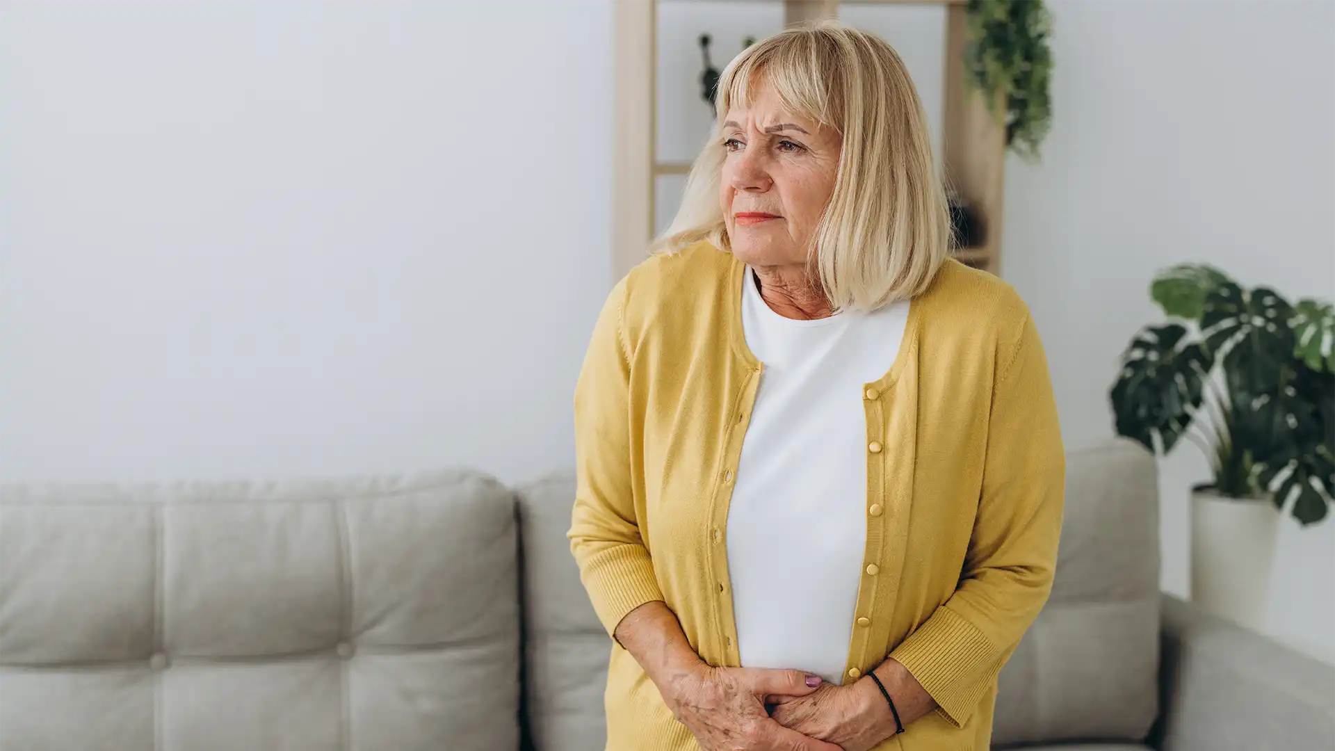 IBS-Relief hypnosis, hypnotherapy, health A woman standing in front of a couch with a stomachache.