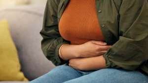 hypnosis, hypnotherapy, health A woman sitting on a couch holding her stomach.