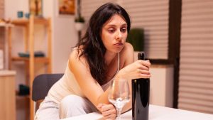 hypnosis, hypnotherapy, health A woman sits quietly at a table, contemplating an unopened wine bottle with an empty glass nearby, reflecting on her alcohol addiction recovery process.