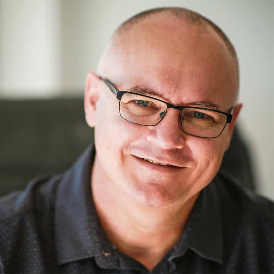 Paul Smith, Sydney's Leading Clinical Hypnotherapist wearing a dark shirt smiles at the camera in a well-lit setting, exuding the confidence often gained through self-hypnosis.