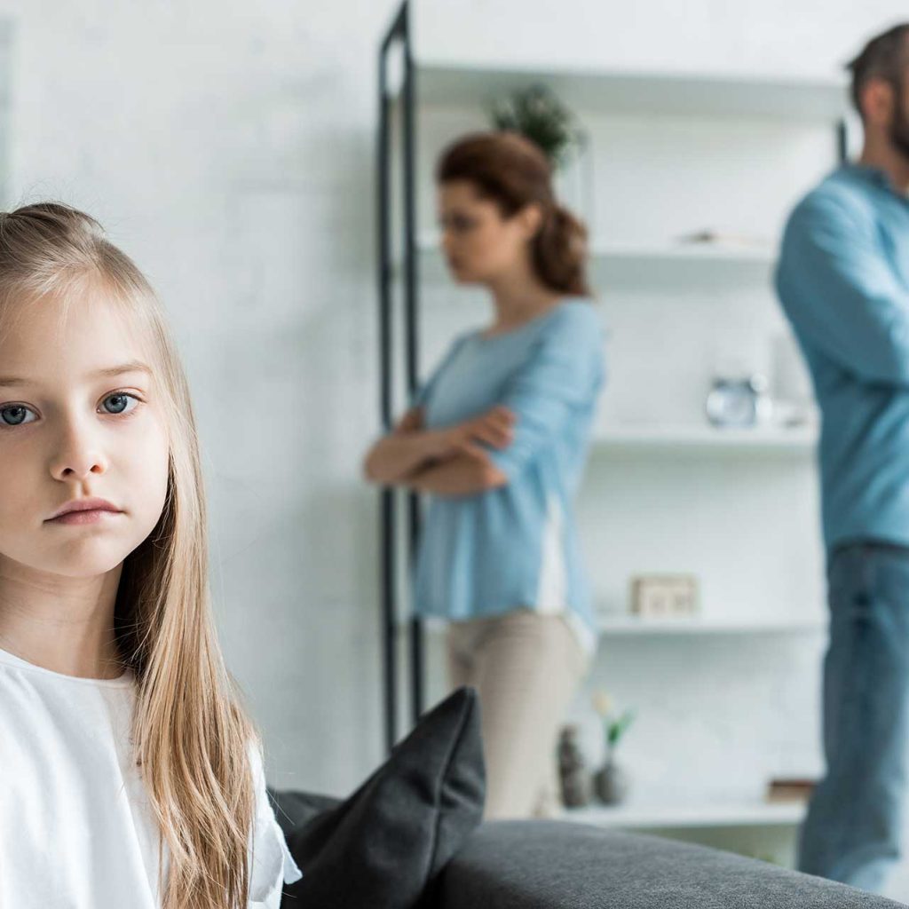 Child looking worried as parents argue in background, illustrating family conflict