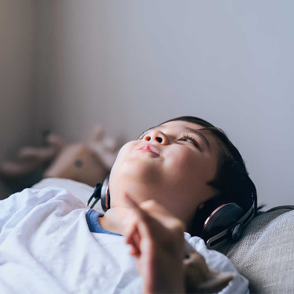 A child wearing headphones lies on a couch, looking up with a relaxed expression, as though immersed in self-hypnosis.