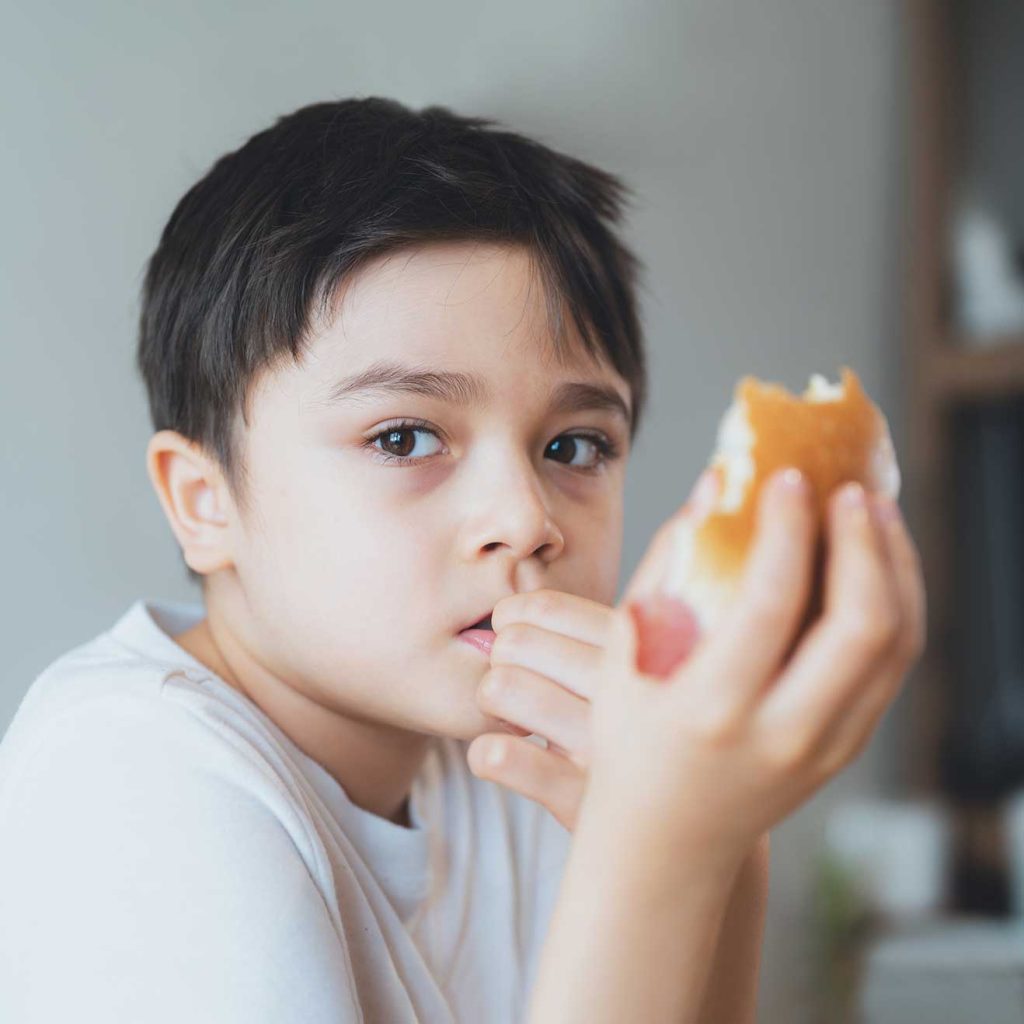 Child with contemplative expression, considering vegetable-filled sandwich