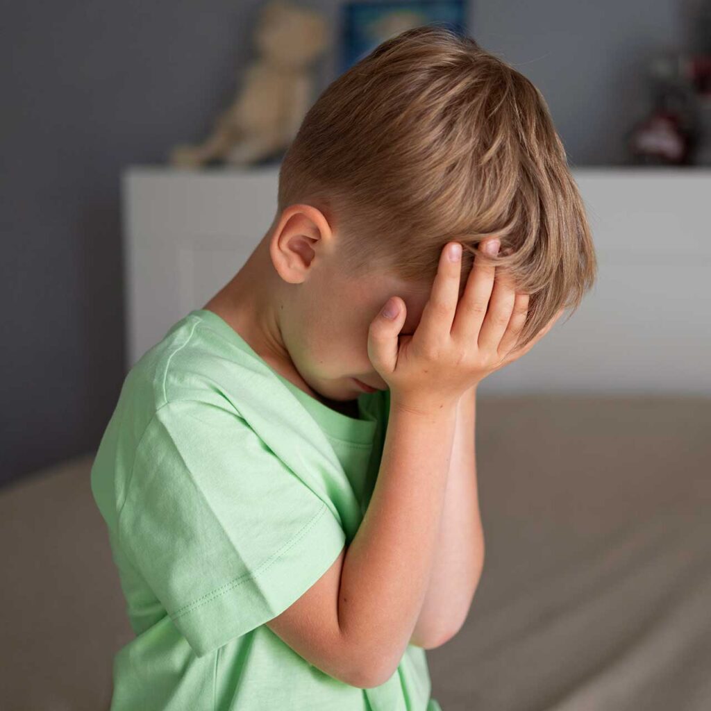 Young boy in green shirt covering face with hands