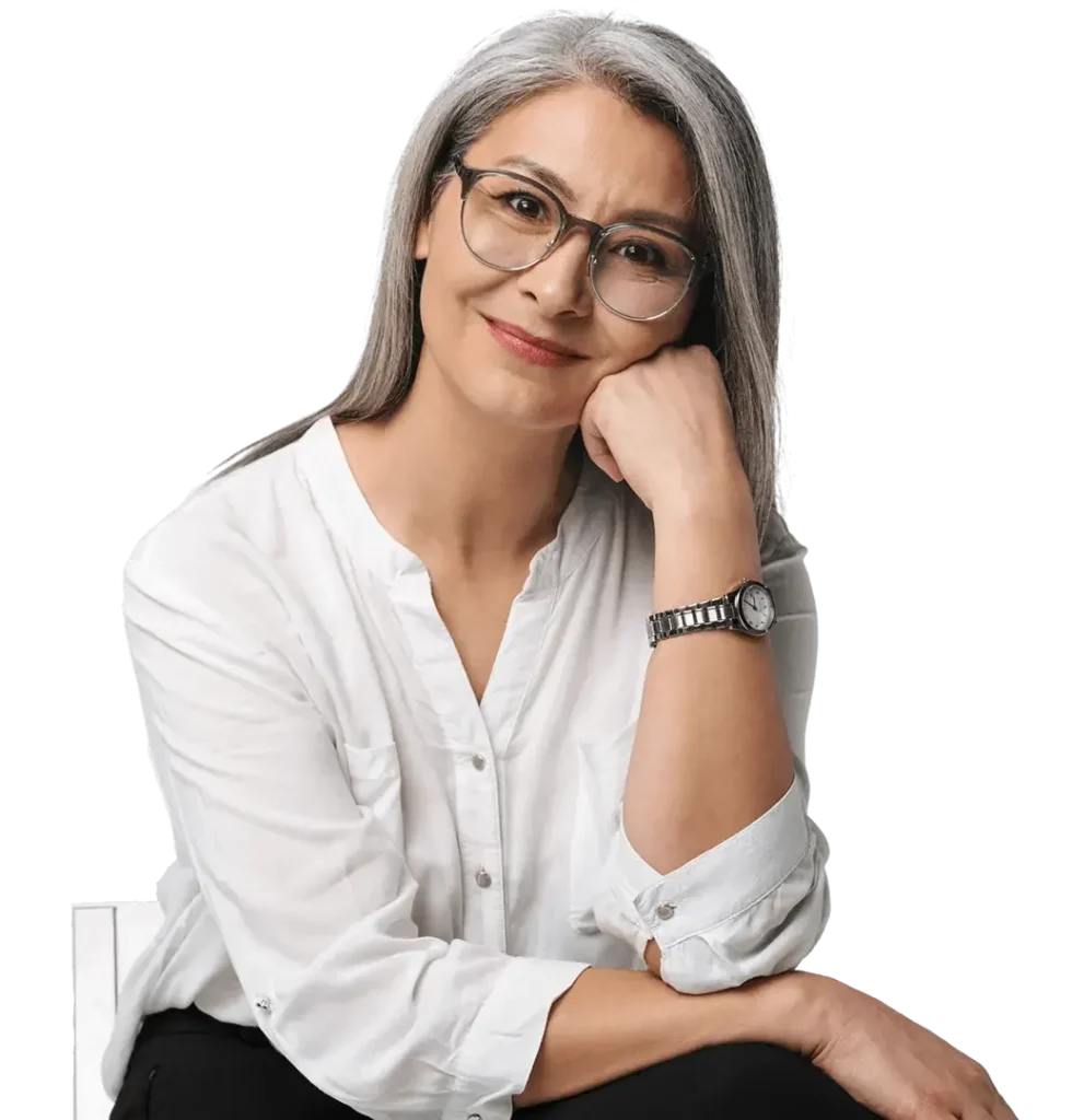 A Middle-Aged Woman With Gray Hair And Glasses, Smiling And Resting Her Chin On Her Hand, Wearing A White Shirt And A Watch.