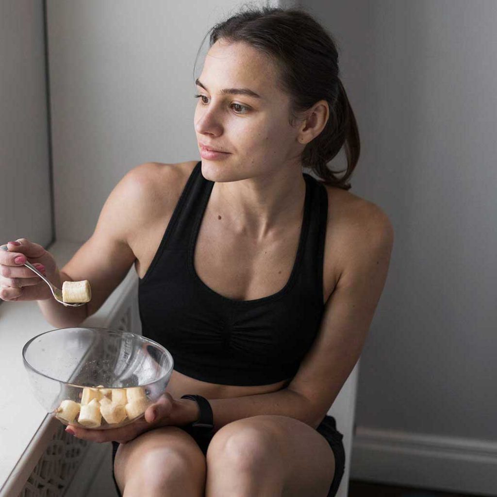 Woman eating banana slices in athletic wear.